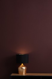 Photo of Wooden table with lamp near brown wall in room, space for text