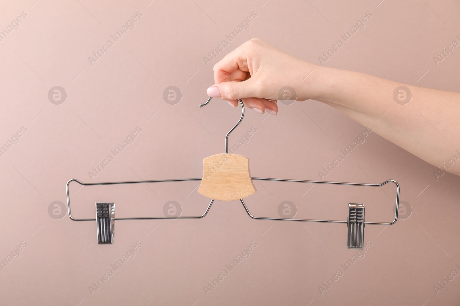 Photo of Woman holding hanger with clips on light brown background, closeup