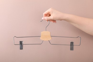 Photo of Woman holding hanger with clips on light brown background, closeup