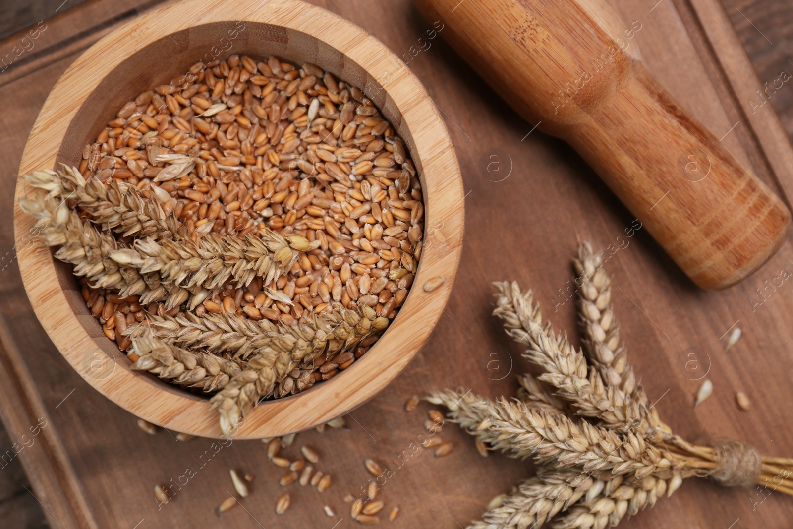 Photo of Mortar, pestle and ears of wheat on wooden table, flat lay