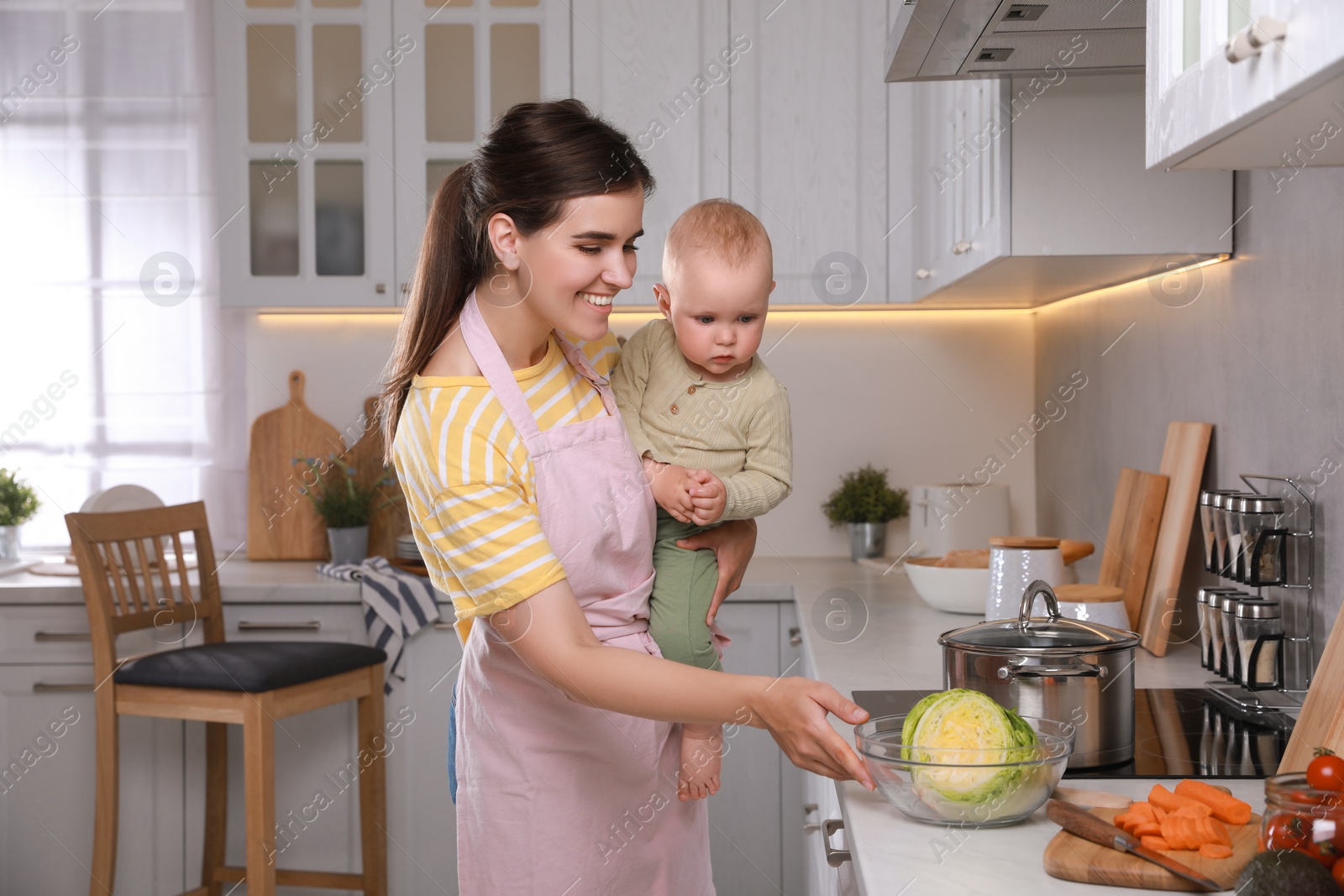 Photo of Happy young woman and her cute little baby spending time together in kitchen