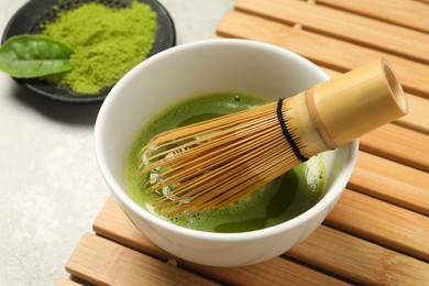Photo of Cup of fresh matcha tea with bamboo whisk on light grey table, closeup