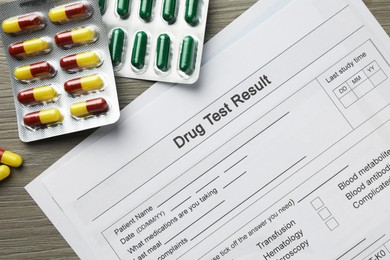 Photo of Drug test result form and pills on wooden table, flat lay