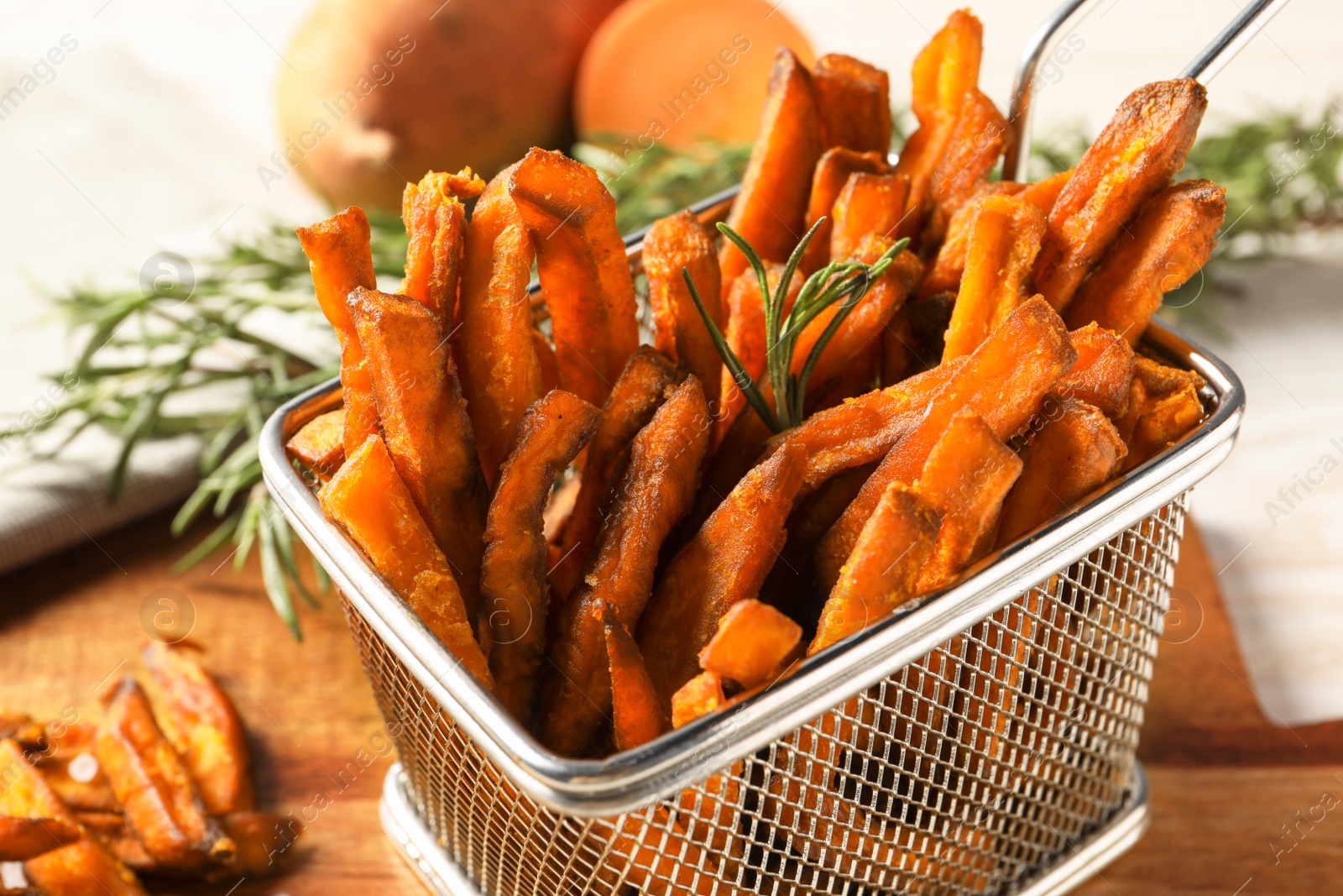 Photo of Frying basket with sweet potato fries and rosemary on wooden table, closeup