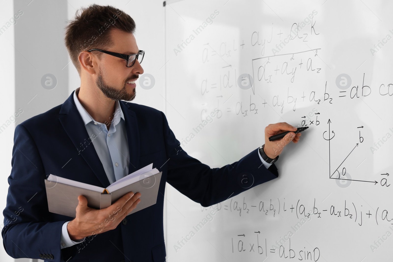 Photo of Happy teacher with book explaining mathematics at whiteboard in classroom