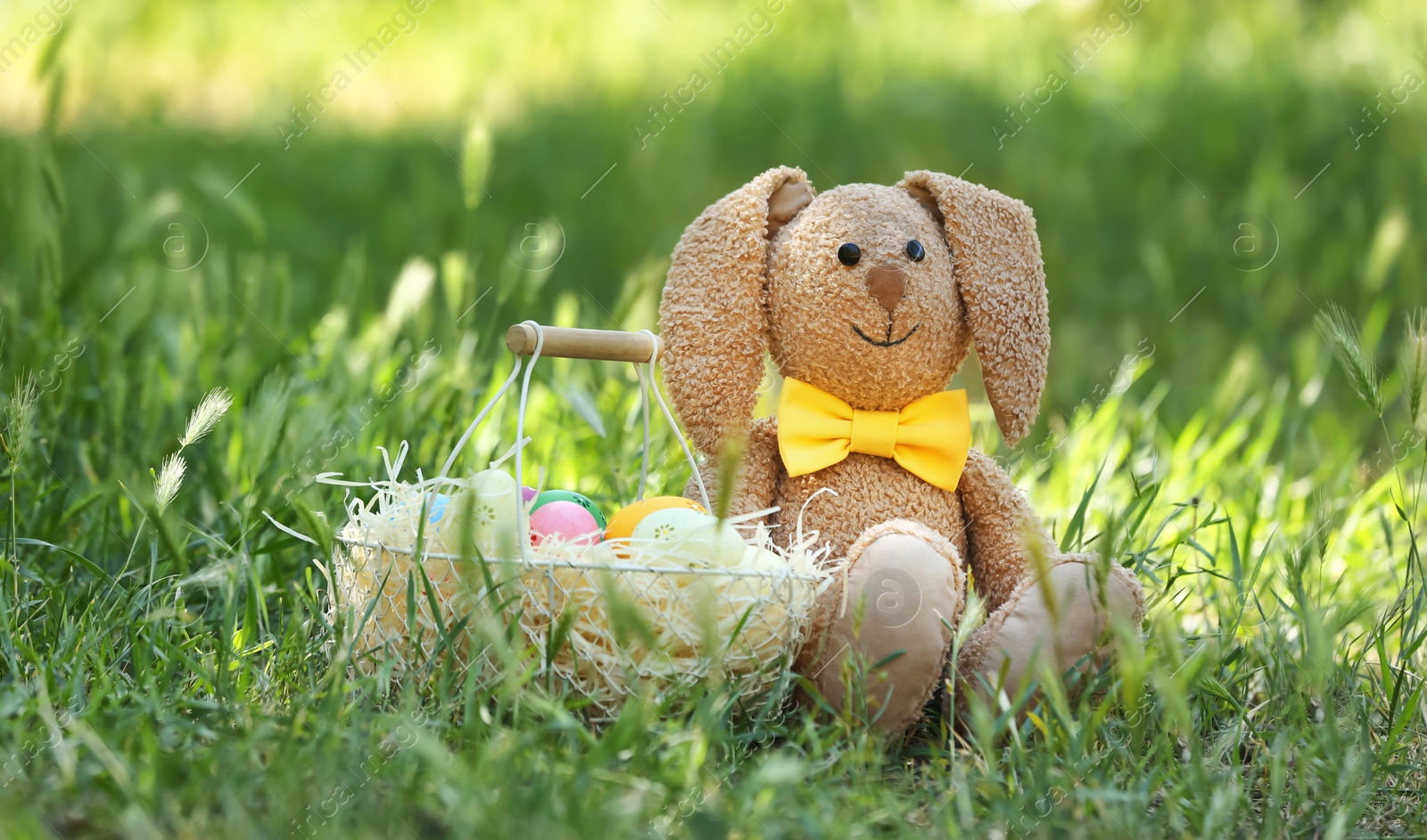 Photo of Toy bunny and basket with Easter eggs on grass