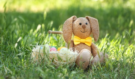 Photo of Toy bunny and basket with Easter eggs on grass