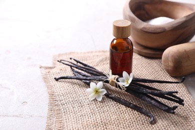 Photo of Vanilla pods, essential oil, flowers and sugar in bowl on light gray table, space for text