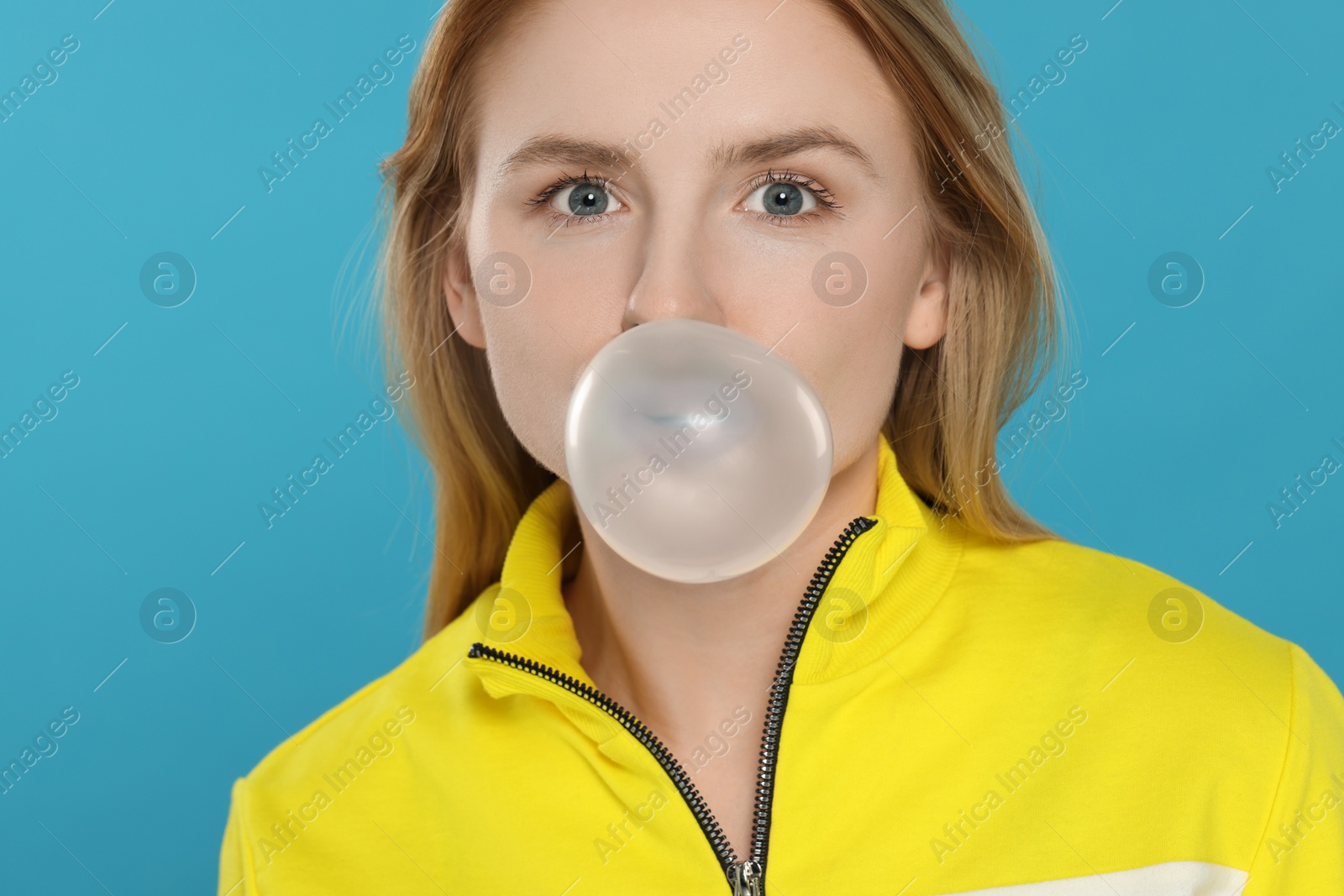 Photo of Beautiful young woman blowing bubble gum on light blue background