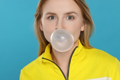 Photo of Beautiful young woman blowing bubble gum on light blue background