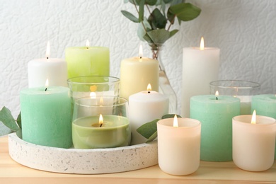 Set of burning candles on table near white wall