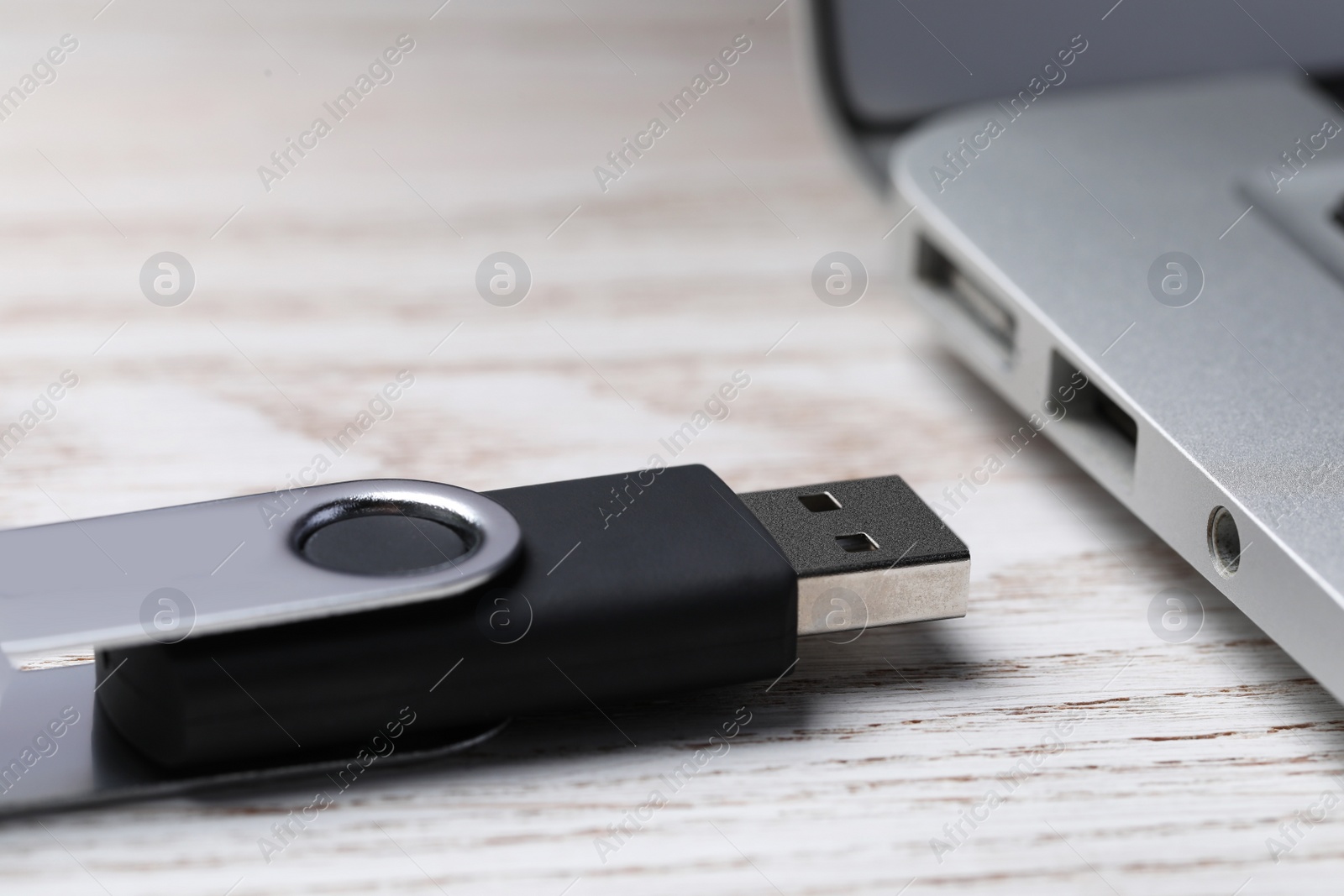 Photo of Usb flash drive near laptop on white wooden table, closeup