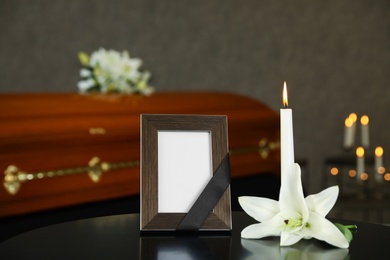 Black photo frame with burning candle and white lily on table in funeral home