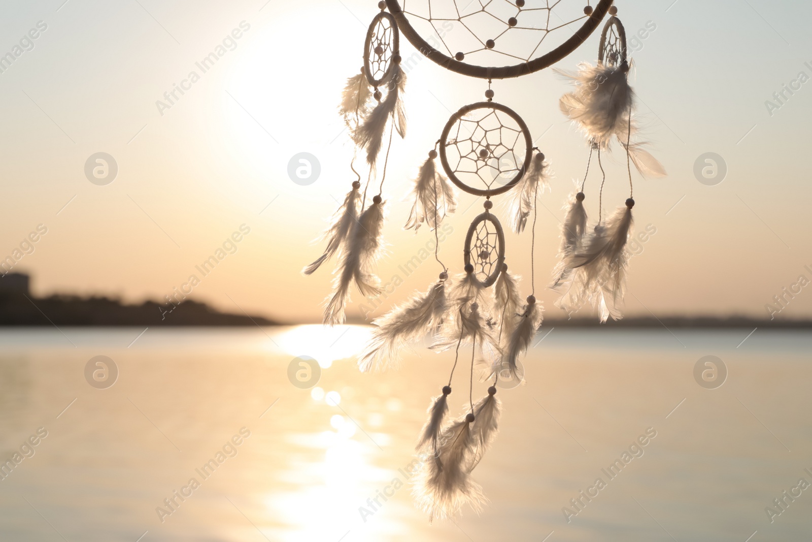 Photo of Beautiful handmade dream catcher near river at sunset. Space for text