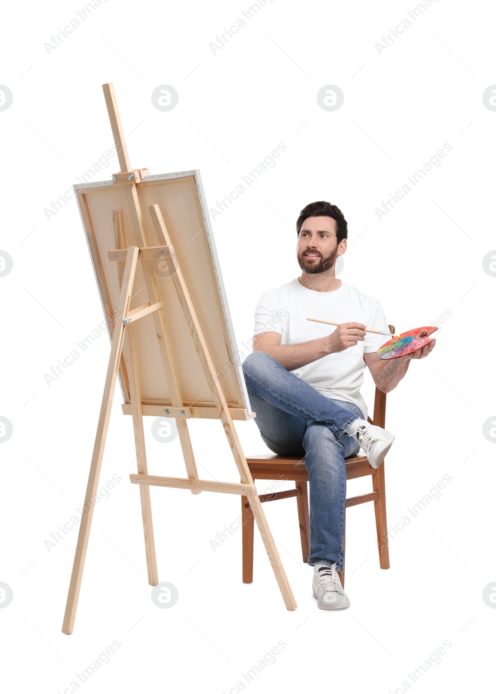 Photo of Man with brush painting against white background. Using easel to hold canvas