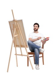 Man with brush painting against white background. Using easel to hold canvas