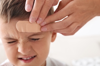 Photo of Woman applying adhesive bandage on boy's forehead indoors, closeup