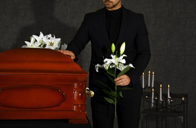 Young man with white lilies near casket in funeral home, closeup