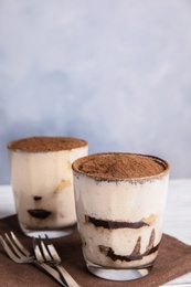 Two glasses of tiramisu cake on table against color background, space for text