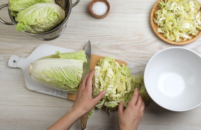 Photo of Woman cutting Chinese cabbage at white wooden kitchen table, top view