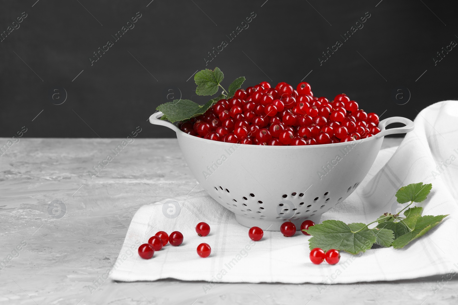 Photo of Ripe red currants and leaves in colander on grey textured table. Space for text