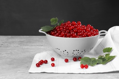 Photo of Ripe red currants and leaves in colander on grey textured table. Space for text