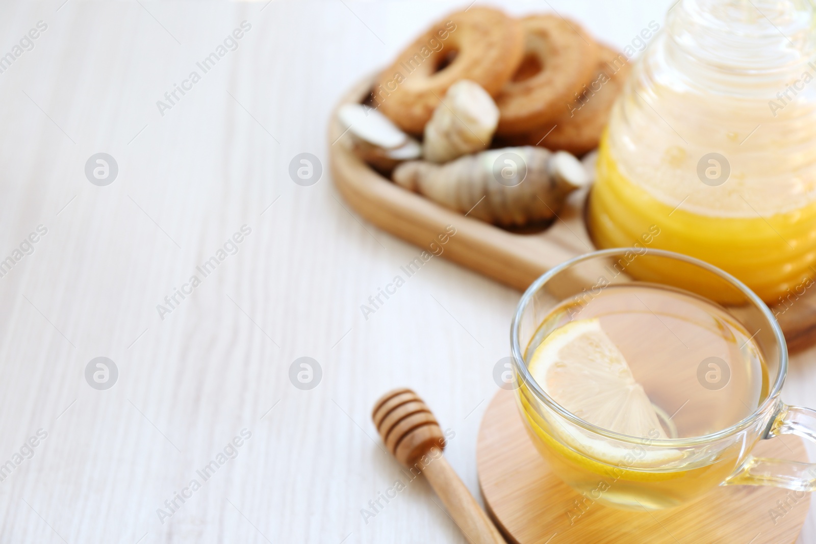 Photo of Cup of delicious tea with lemon, honey and ginger on white wooden table. Space for text