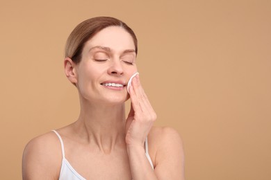 Beautiful woman removing makeup with cotton pad on beige background, space for text