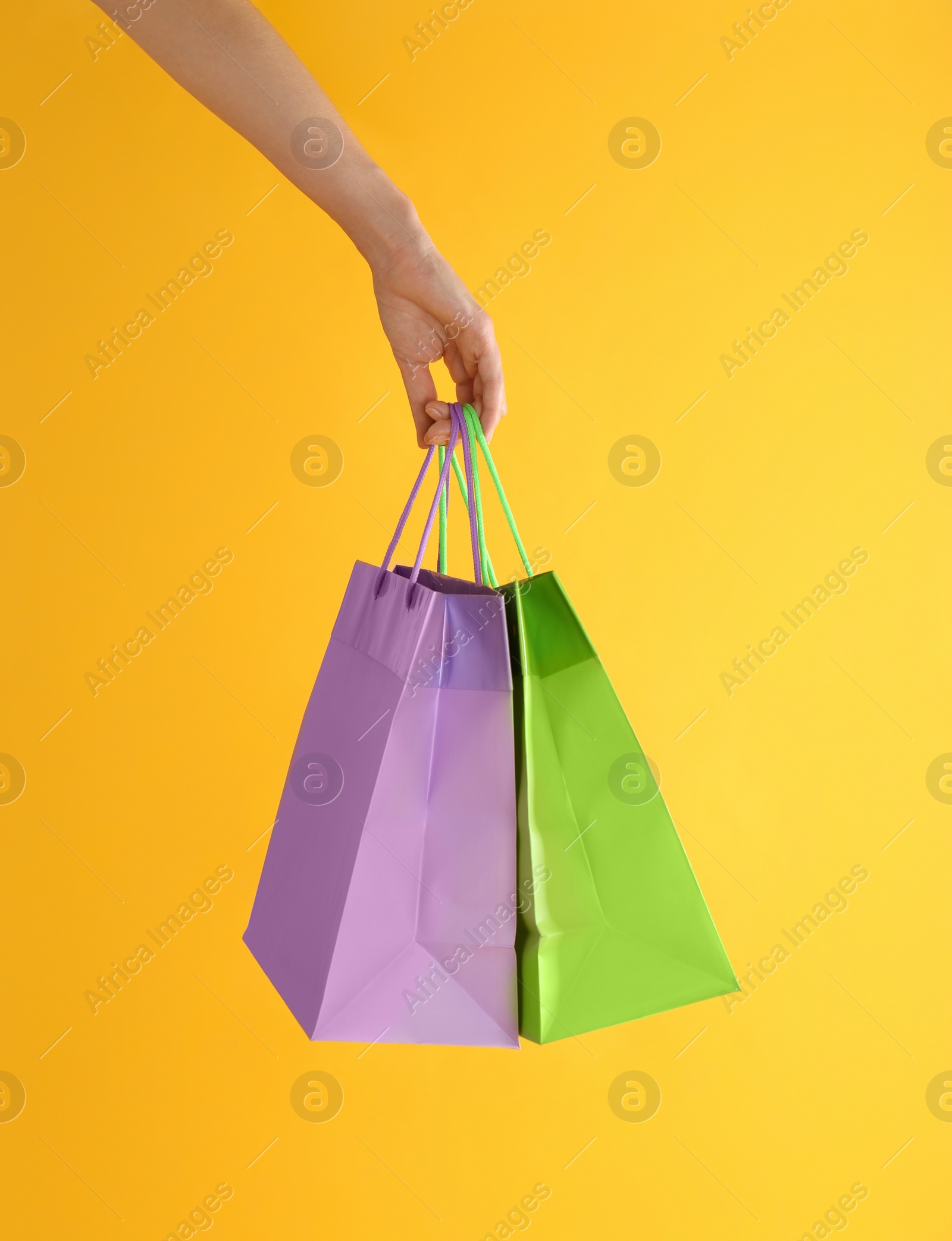 Photo of Woman with paper shopping bags on yellow background, closeup