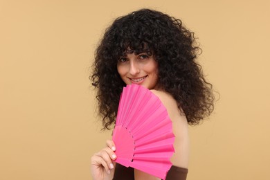 Happy woman holding hand fan on beige background