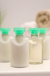 Mini bottles of cosmetic products on white table against blurred background, closeup