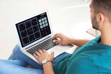 Man playing sudoku game on laptop indoors, closeup