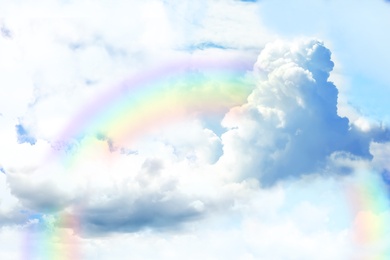 Fantasy world. Beautiful rainbow in sky with fluffy clouds