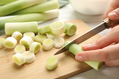 Photo of Woman cutting fresh raw leek on wooden board at table, closeup