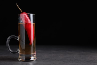 Photo of Red hot chili peppers and vodka in shot glass on grey table against black background, space for text