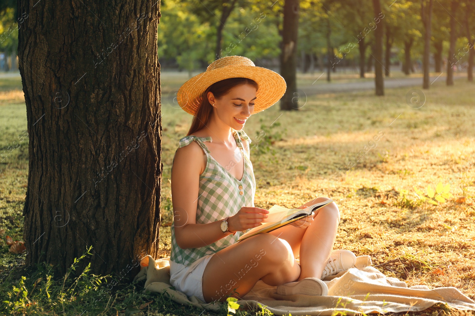 Photo of Young woman reading book on green grass near tree in park