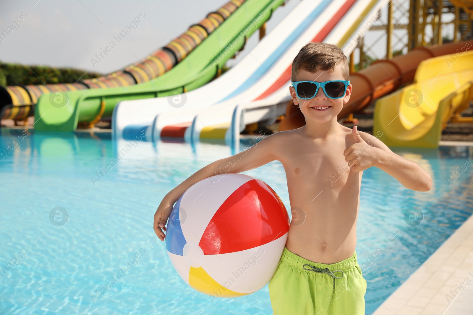 Photo of Cute little boy with inflatable ball near pool in water park, space for text