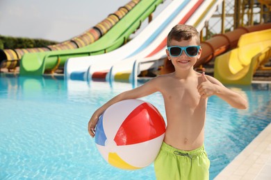 Cute little boy with inflatable ball near pool in water park, space for text
