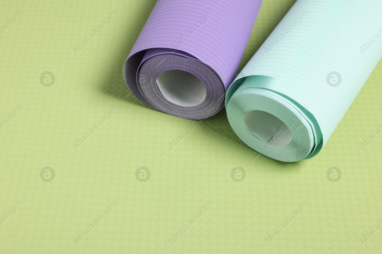 Photo of Two colorful wallpaper rolls on green sample, space for text