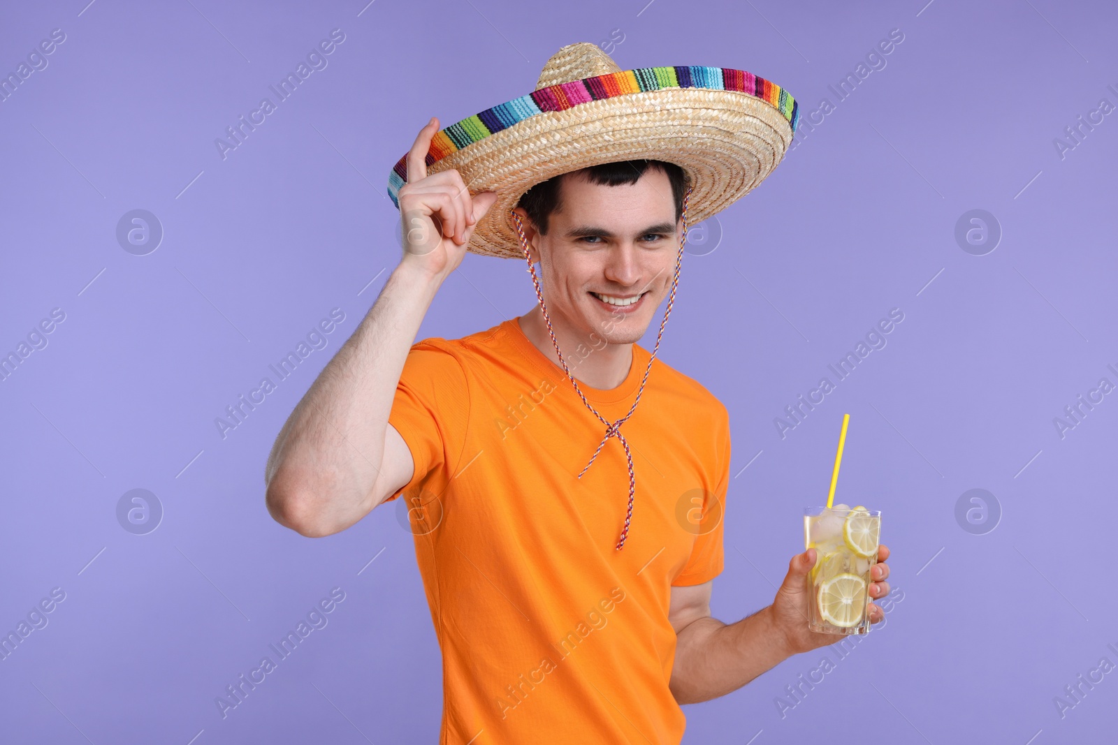 Photo of Young man in Mexican sombrero hat with cocktail on violet background