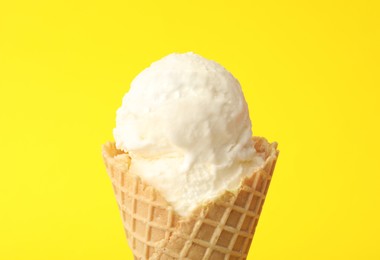 Photo of Delicious ice cream in waffle cone on yellow background, closeup