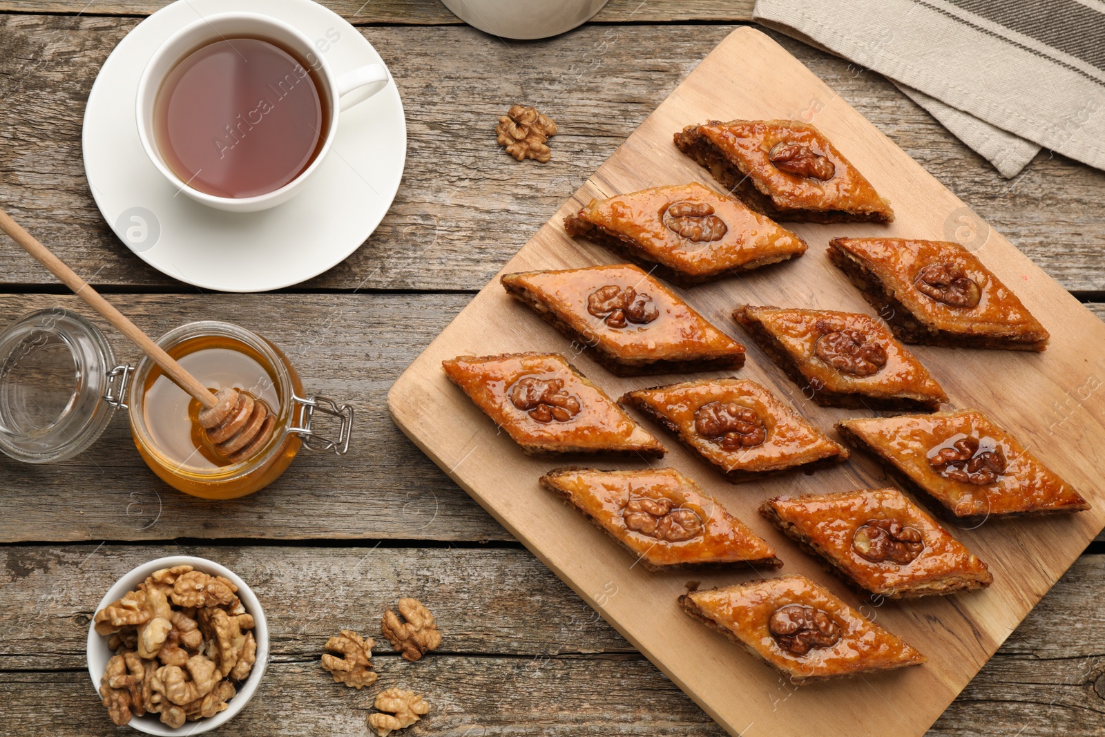 Photo of Delicious sweet baklava with walnuts, honey and hot tea on wooden table, flat lay