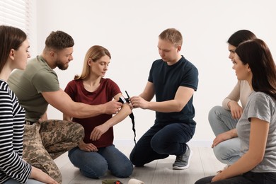 Photo of Soldier in military uniform teaching group of people how to apply medical tourniquet indoors