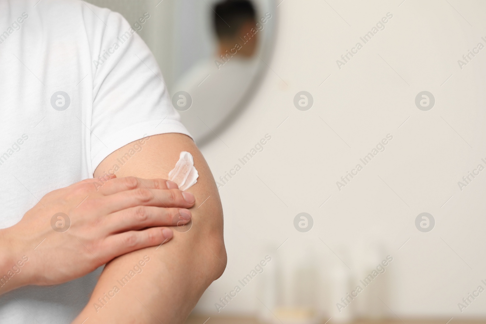 Photo of Man applying body cream onto his arm indoors, closeup. Space for text