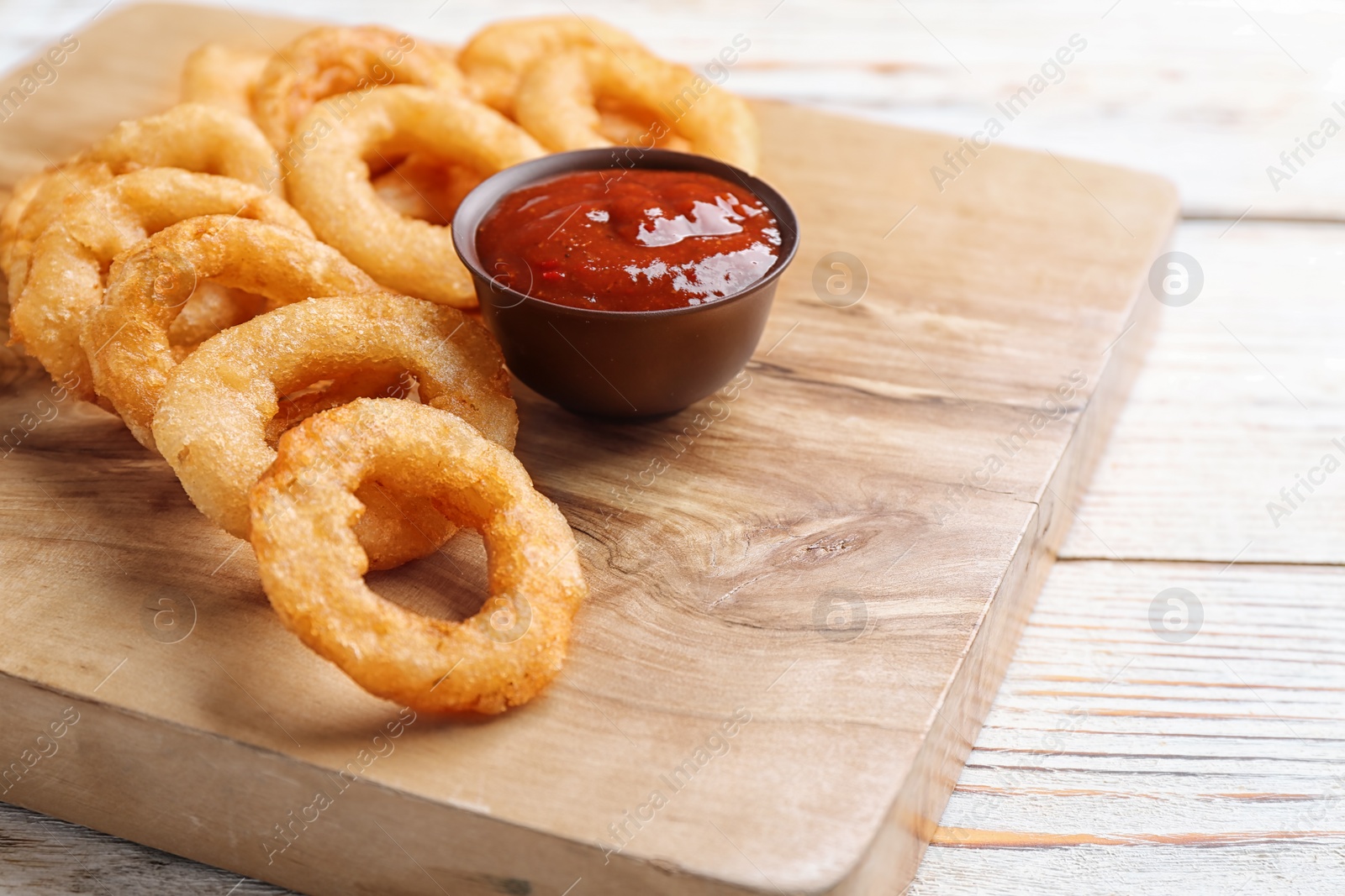 Photo of Fried onion rings served with sauce on wooden board, closeup