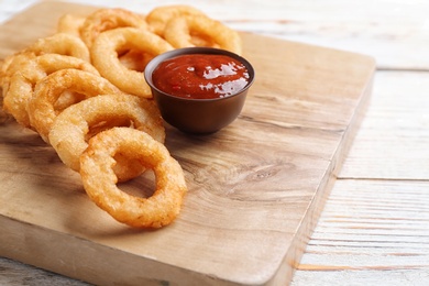 Fried onion rings served with sauce on wooden board, closeup