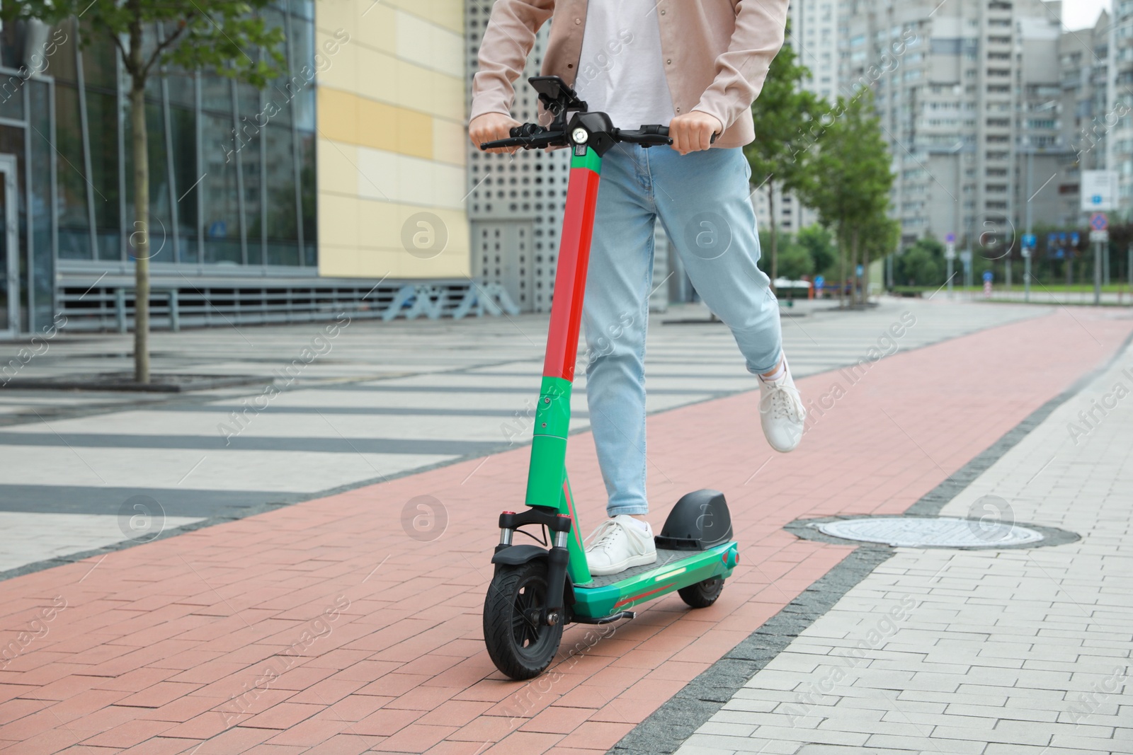 Photo of Man riding modern electric kick scooter on city street, closeup