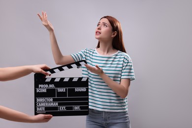 Photo of Emotional actress performing role while second assistant camera holding clapperboard on grey background