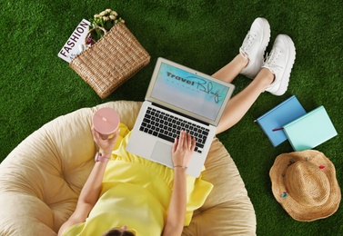 Woman and laptop with travel blogger site on artificial grass, top view