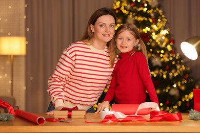 Photo of Christmas presents wrapping. Mother and her little daughter at table with gift boxes, decor in room